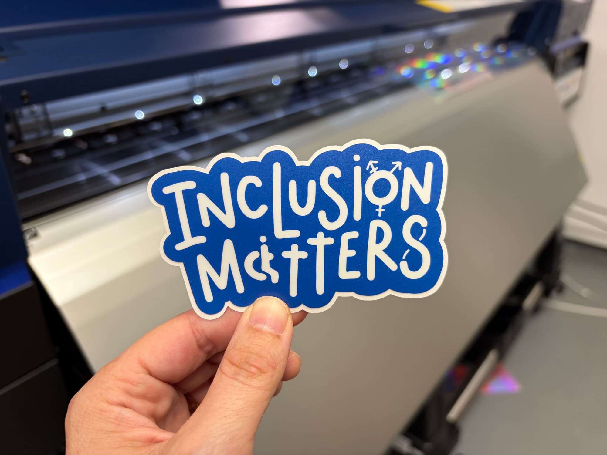 A blue 'Inclusion Matters' die cut sticker with disability and transgender symbols worked into the lettering