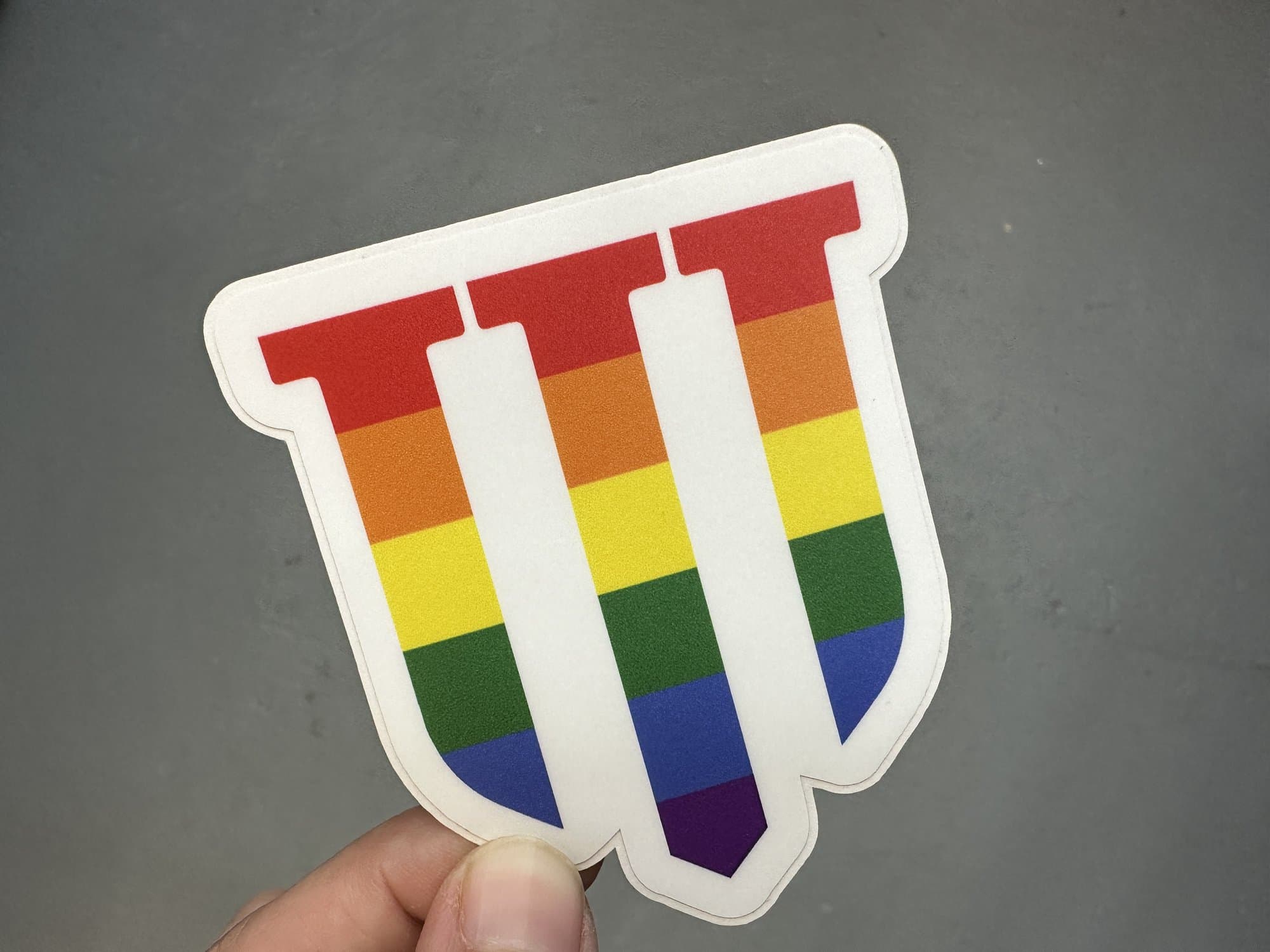 A rainbow shield die cut sticker with three white pillars