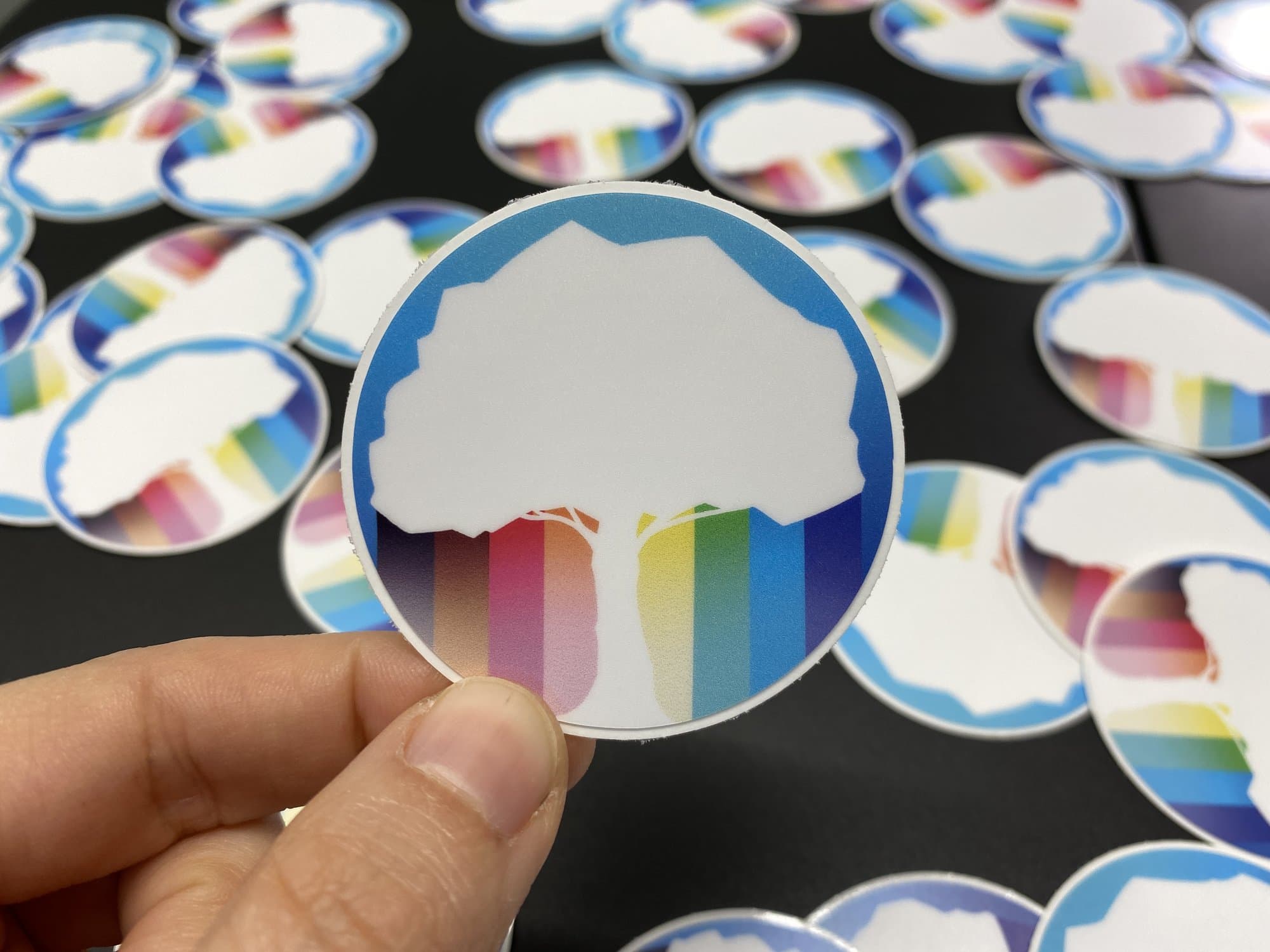 Circle stickers with a tree silhouette over rainbow and trans flag colors